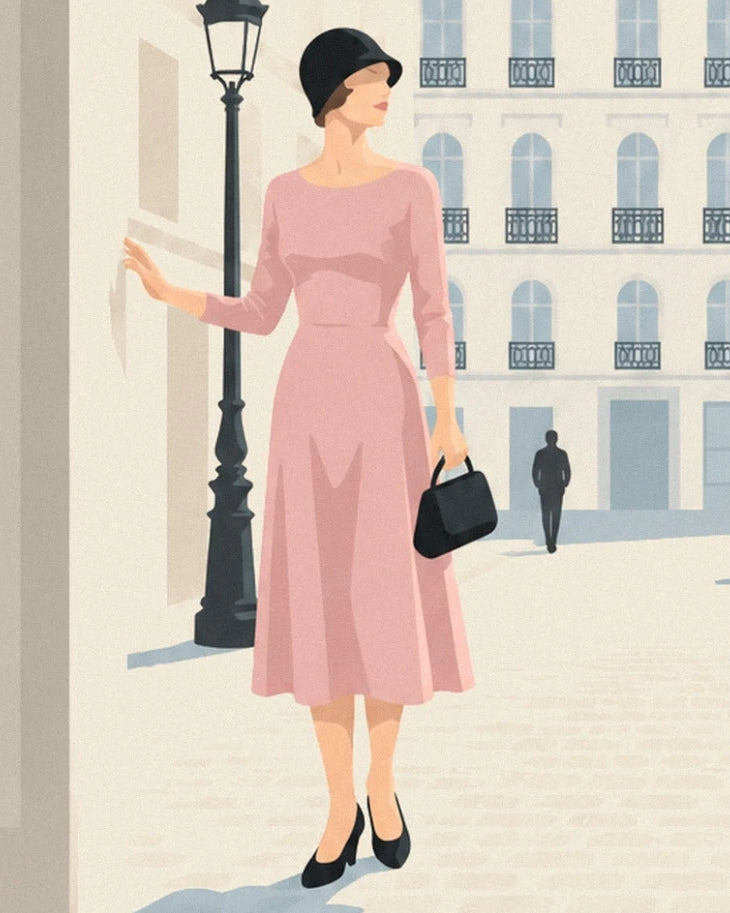 Une femme en robe rose, chapeau et sac noirs près d’un réverbère, devant une façade claire