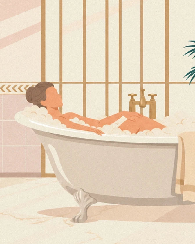 The woman with her hair in a bun reclining in her freestanding bath, with bubbles and a golden tap