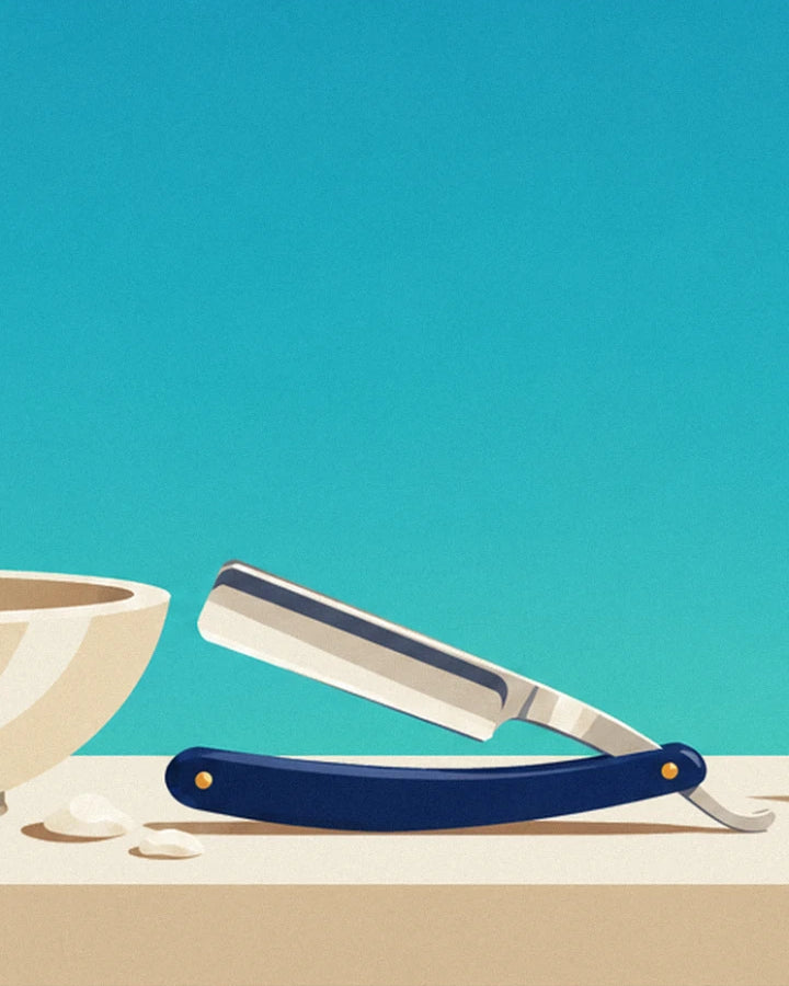 The straight razor with a blue handle resting beside the bowl, with a few dabs of foam