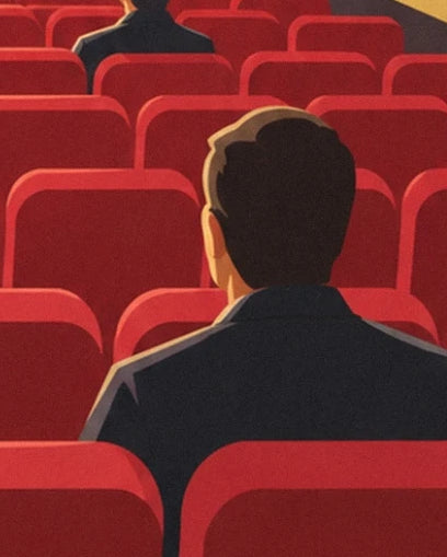 A cinema-goer in a dark jacket seen from behind among the red cinema seats